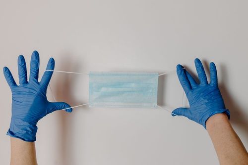 Hands in blue gloves holding a surgical face mask